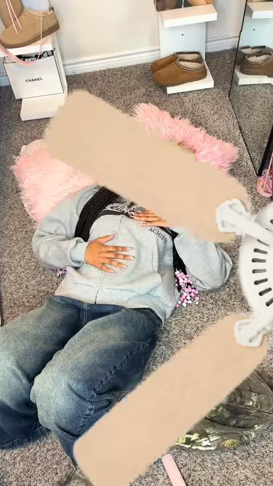 Overhead view of a woman in a light-blue hoodie and baggy jeans on a grey carpet with a beige fan blade crossing her face