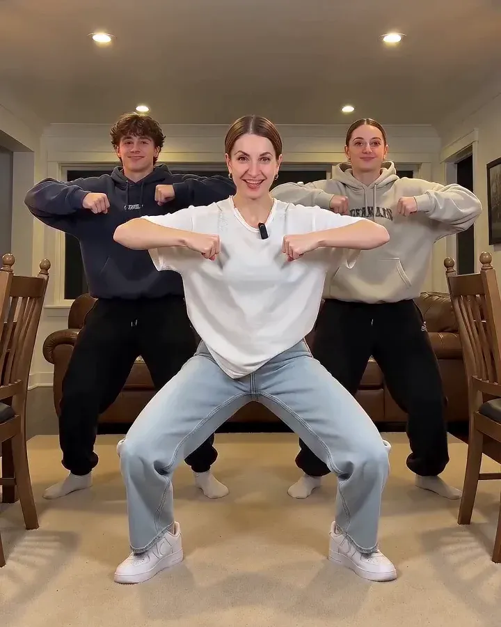 Three dancers in a living room sinking into a deep wide squat with fists pulled in to the chest