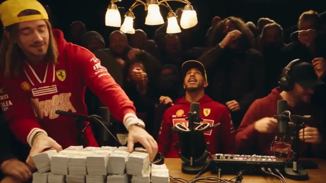 The standing performer leans over the wooden table and pushes the stacks of cash forward with both hands while his seated partner and the crowd watch
