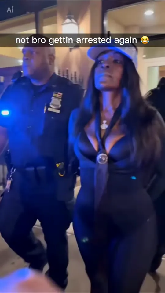 A woman in a light blue cap and black outfit walks along a night sidewalk beside a police officer, with the meme caption on screen