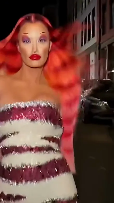 Shot two of a ramalama costume walk: the camera pulls back to reveal a woman with long red hair, purple eye makeup and bold red lips in a strapless sequined gown