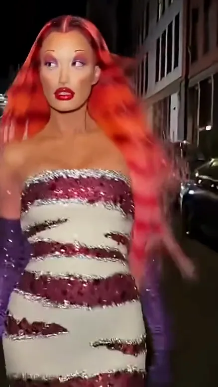 Final beat of a ramalama costume walk: the red-haired woman strides toward the camera with purple gloves swinging and hair flying