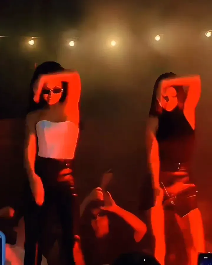 Two dancers in sunglasses sweep one forearm across over their eyes