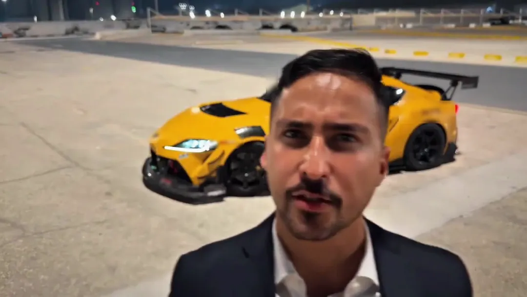 A yellow sports car with a tall rear wing is now parked behind the man as he talks into the camera