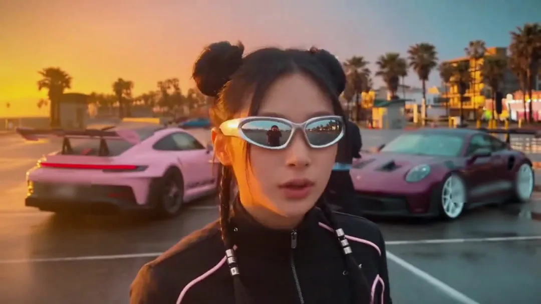 The cards are gone and a pink sports car and a dark purple sports car are parked behind her under palm trees